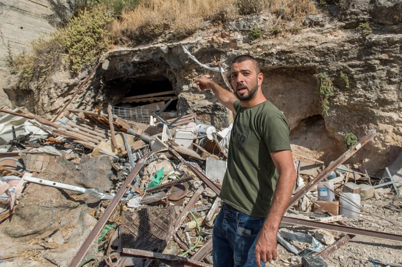 A man points to some rubble behind him