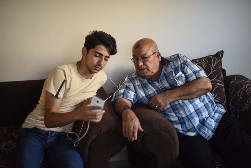 Two men share ear buds as they look at phone