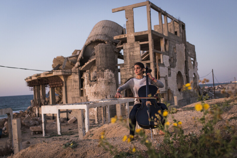A woman plays the cello in front of the rubble of a destroyed building