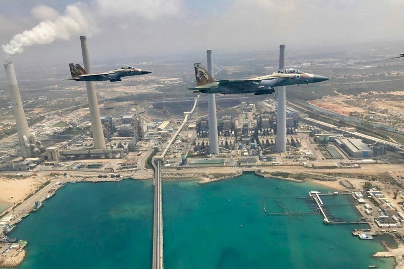 Two warplanes against backdrop of smoke stacks and industrial buildings