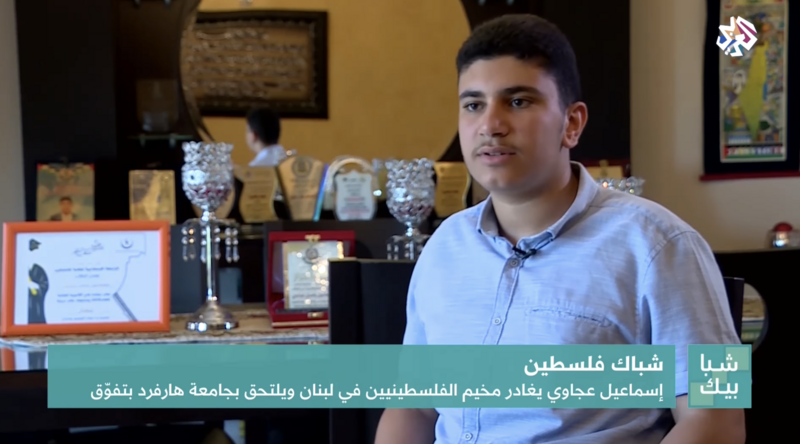 A young man sits in front of awards on a shelf.