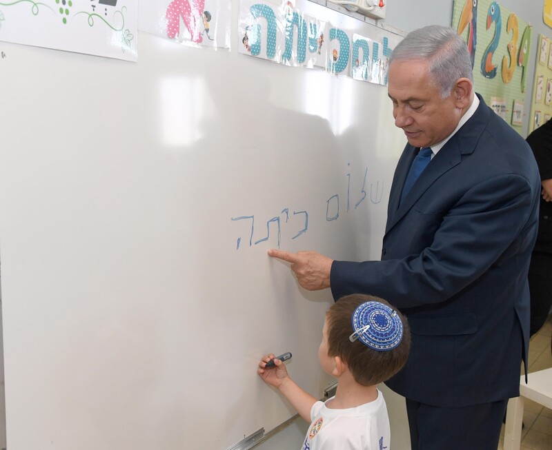 Man in suit looks over a child as he writes on a whiteboard