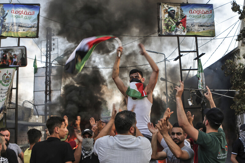 Man holding Palestinian flag carried by other men with backdrop of smoke