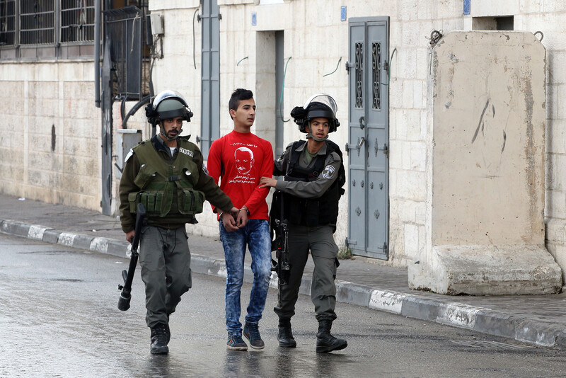 Two soldiers walk with handcuffed youth between them