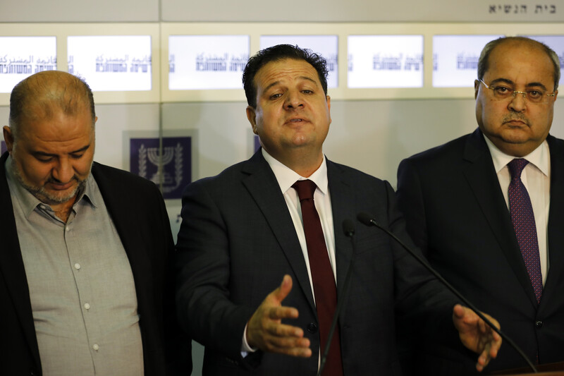 One besuited man, flanked by two others, gestures as he speaks.