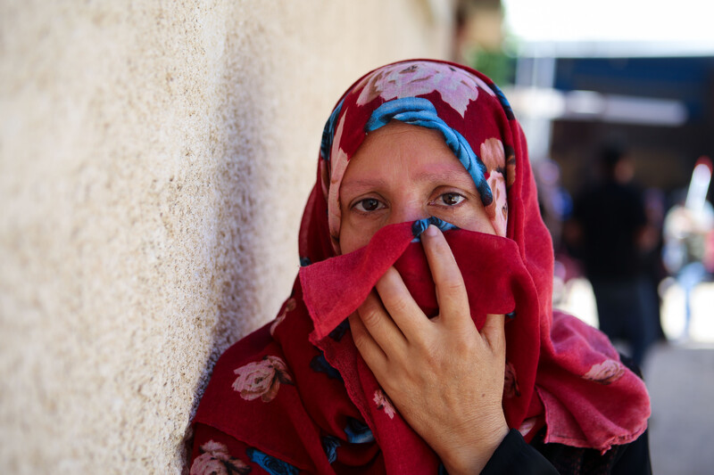 A woman holds a deep red veil up to her face.