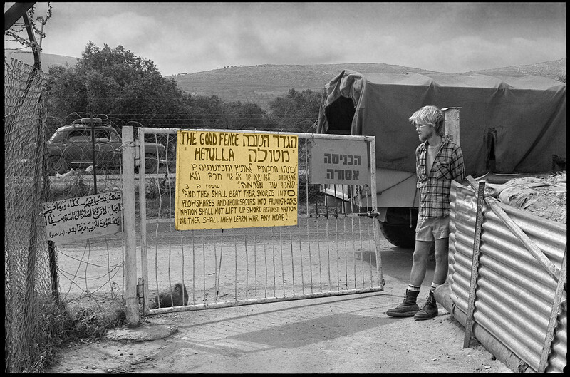 Young man stands in front of gate with sign reading The Good Fence