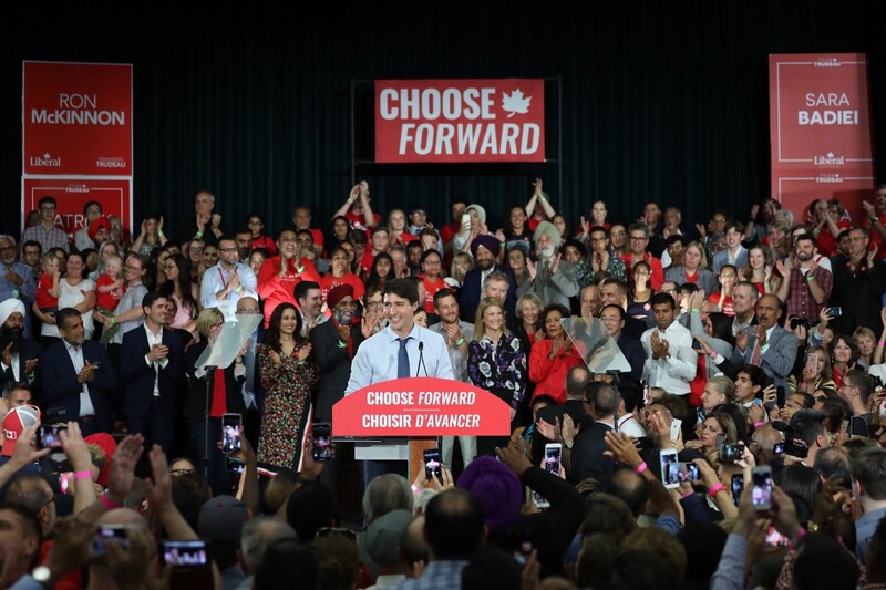 Man surrounded by crowd and signs speaks at podium