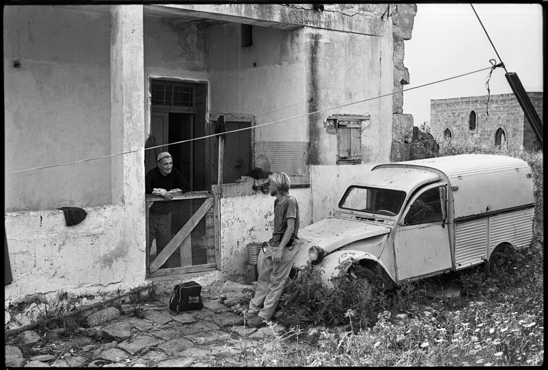 Young man leaning against car talks to an older man over a fence