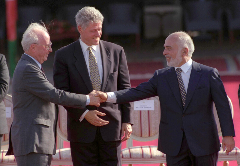 One man watches two others shake hands.