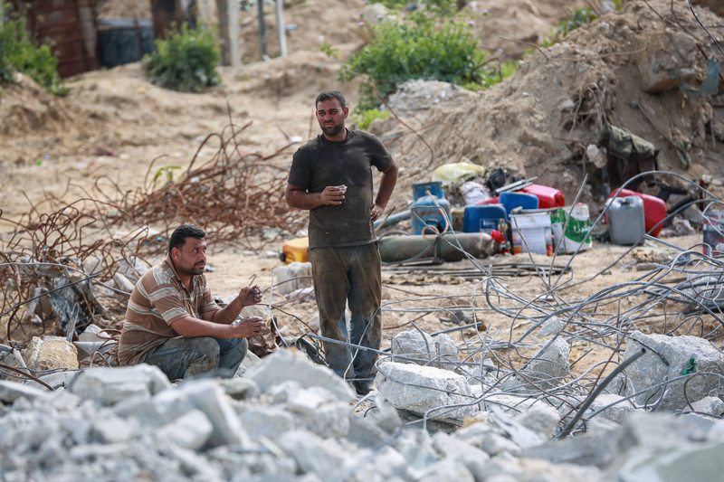 Two men enjoy a break in the middle of some rubble, both holding plastic cups of coffee