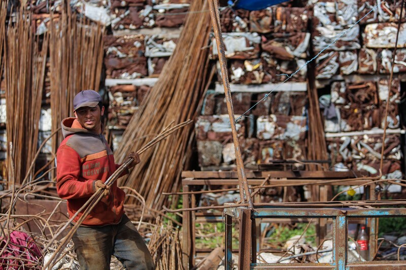 A man carries steel bars with bare hands in a yard filled with similar bars