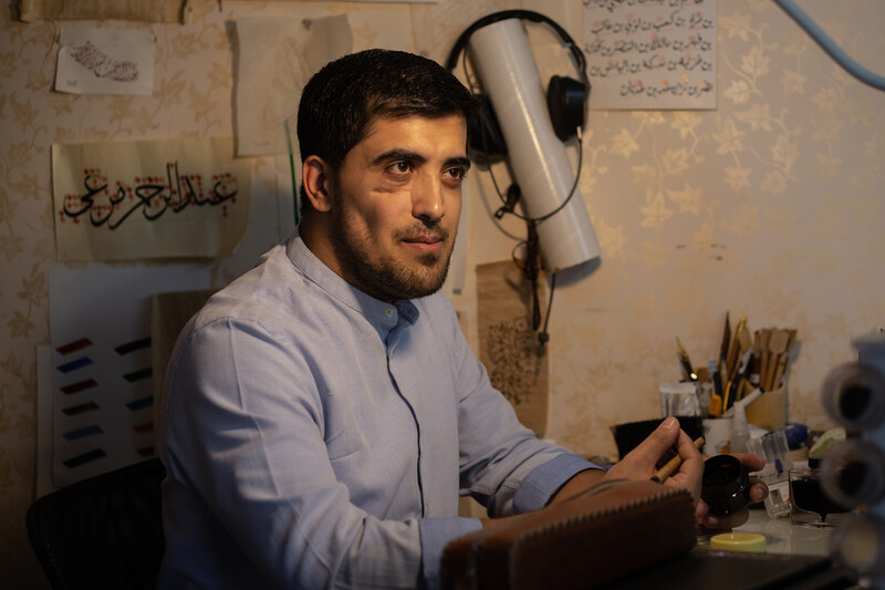 A man sits behind a desk, smiles 