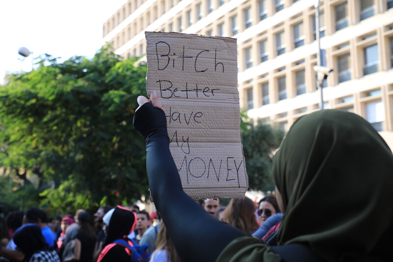 A woman seen from the back holds up a sign written in English.