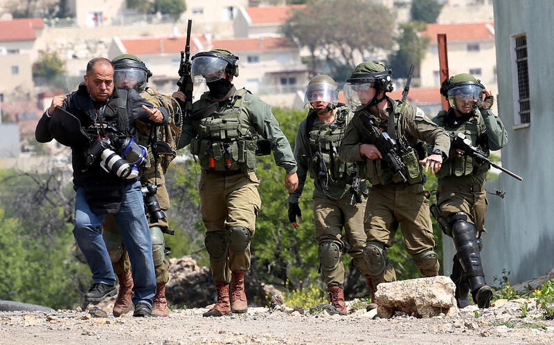 A man with cameras around his neck is being accosted by five uniformed soldiers.