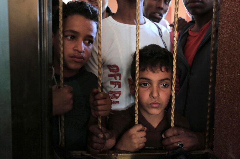 Two boys stare through bars in a window