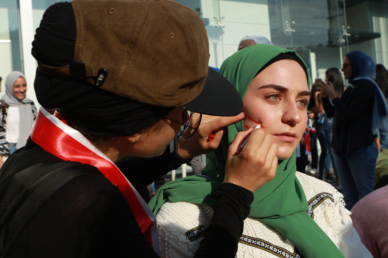A woman is drawing red lines on the cheek of another woman.