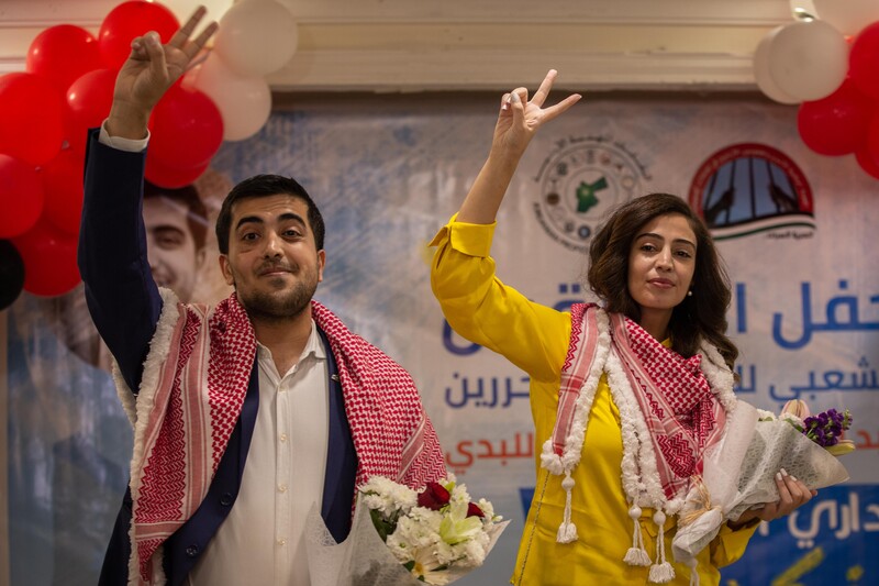 A man and a woman smile, make peace sign with their right hands