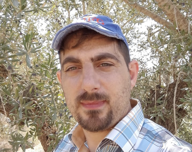 Man wears a cap standing in front of olive branches