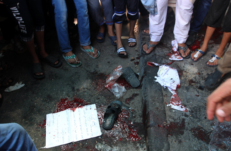 People seen from legs down stand around blood-stained street