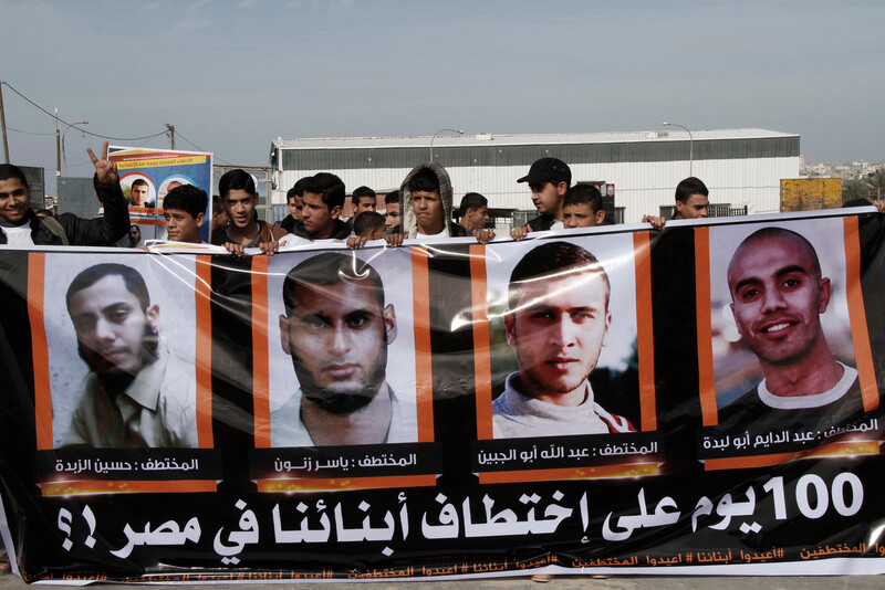 People hold up posters with the pictures of four men.