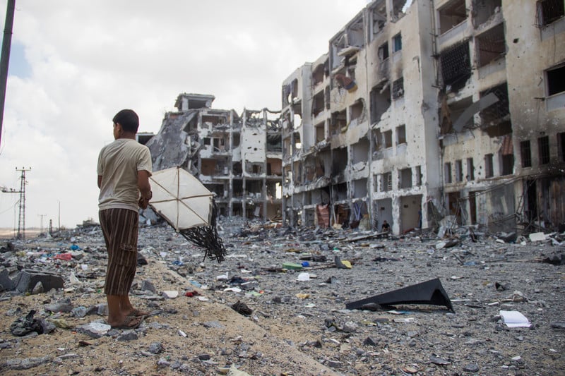 Boy holds kite in front of bombed-out multi-story buildings