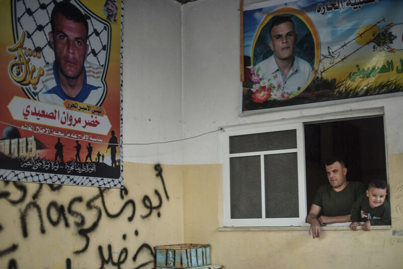 Man and child look out the window, posters on the walls surround them