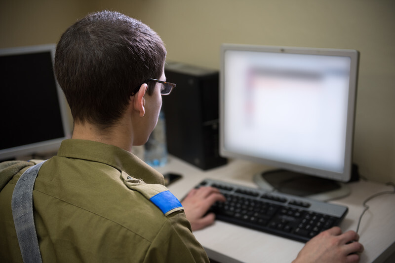 Man in military uniform sits in front of computer