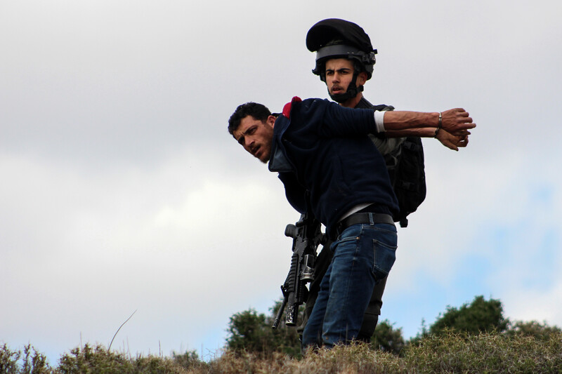A soldier restrains a man who is in handcuffs