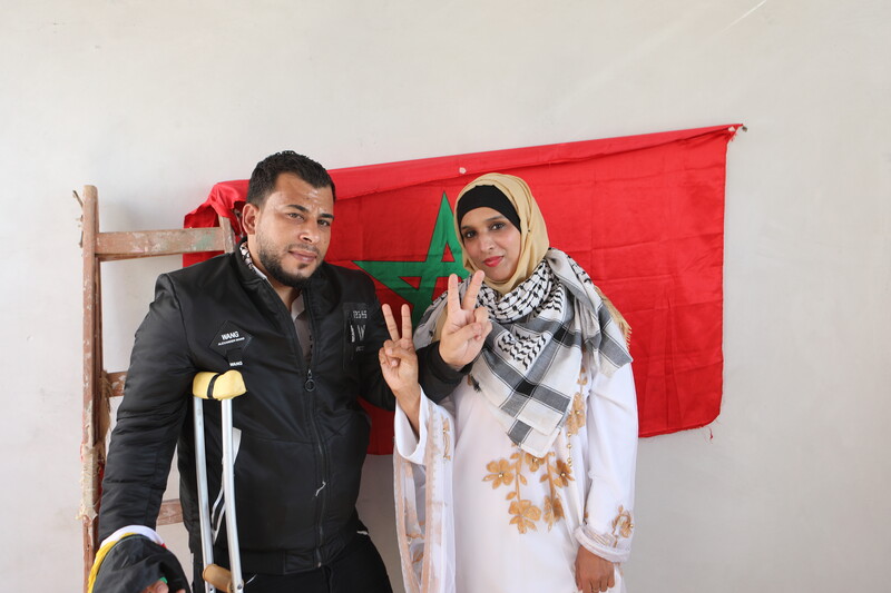 A couple flash the victory sign in front of a Moroccan flag.