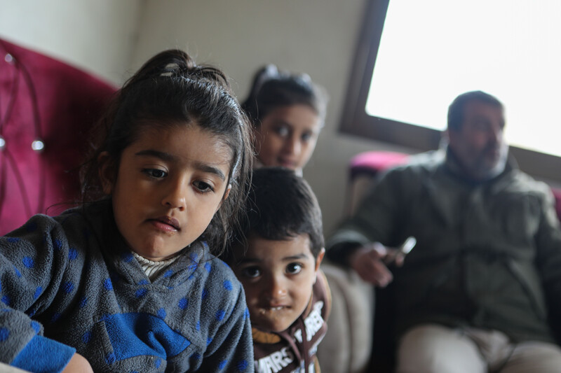 Three small children stand in foreground as man sits behind them