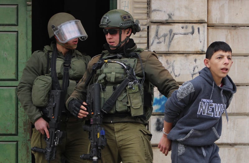 Two full armed soldiers holding handcuffed boy 