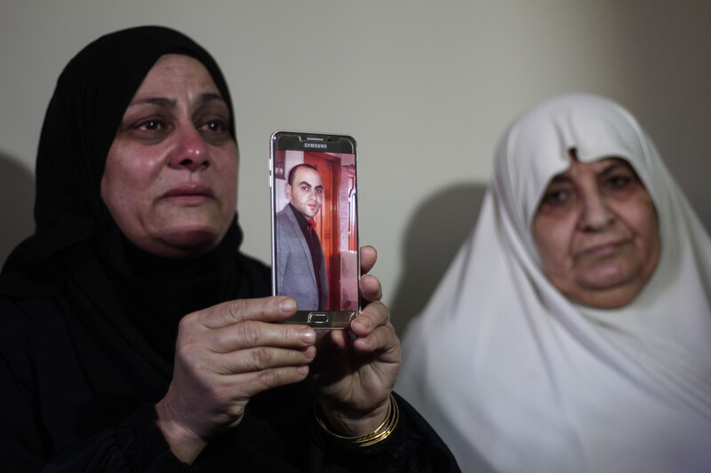 Two women cry, one holds up a picture of a man displayed on a phone