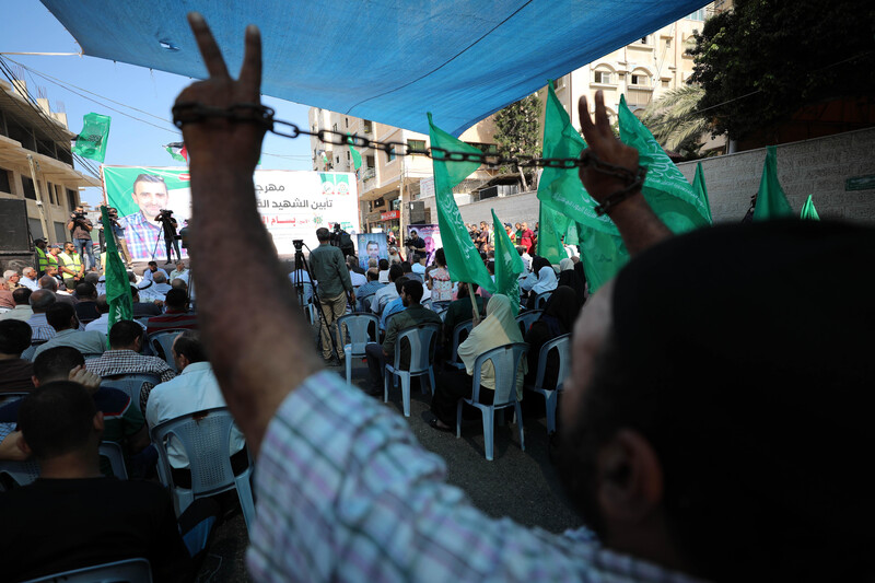 A man flashes a v-sign behind a number of people seated beneath a poster.