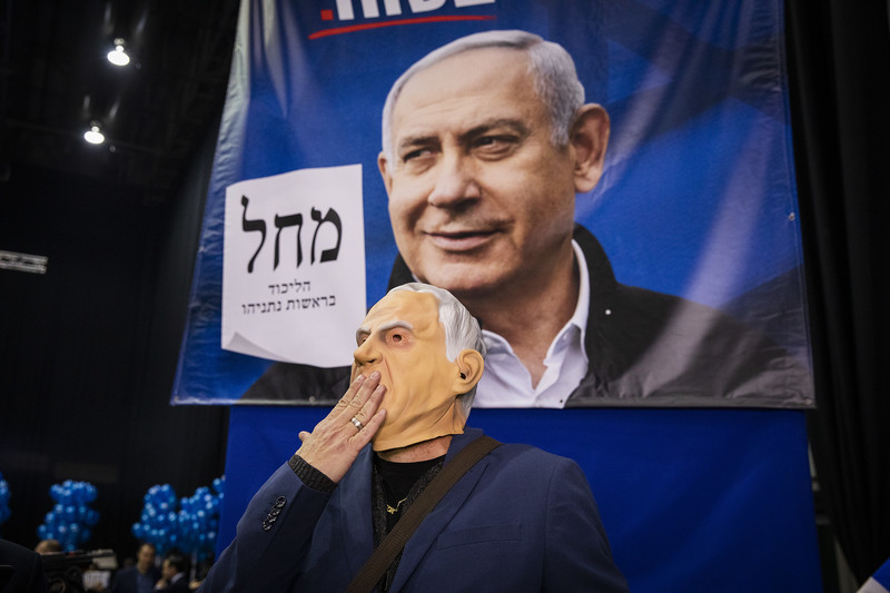 a person wearing a mask stands before an election poster