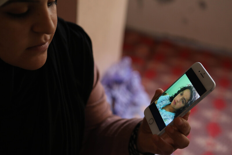 A woman holds a phone showing a picture of herself as a young girl