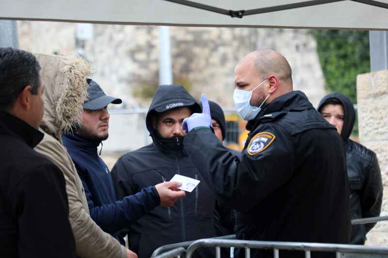 A uniformed man in a protective face mask raises his index finger at a group of men without masks