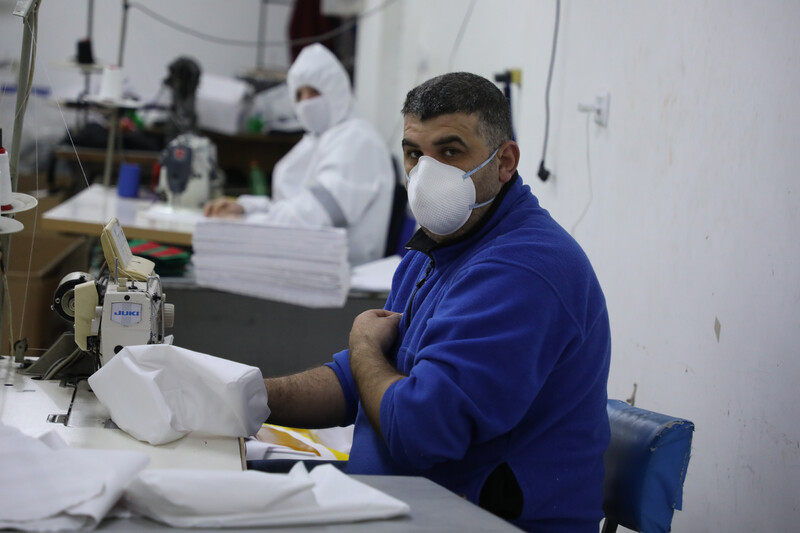 People wearing protective gear work at sewing machines