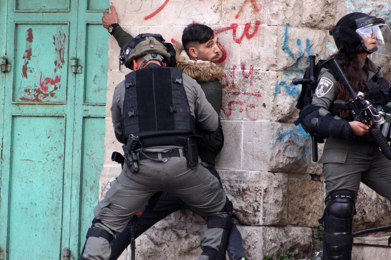 A soldier pins a young man against a stone wall
