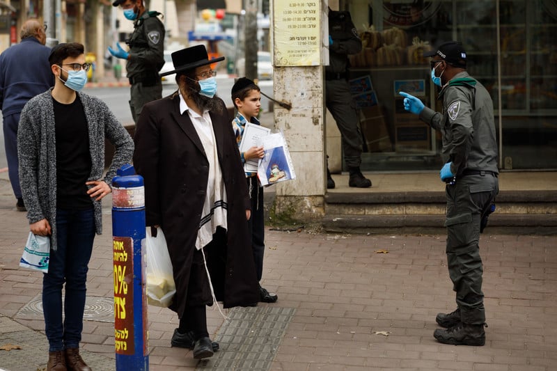 An Israeli policeman in a face mask gestures at two men, also in face masks, and one boy without