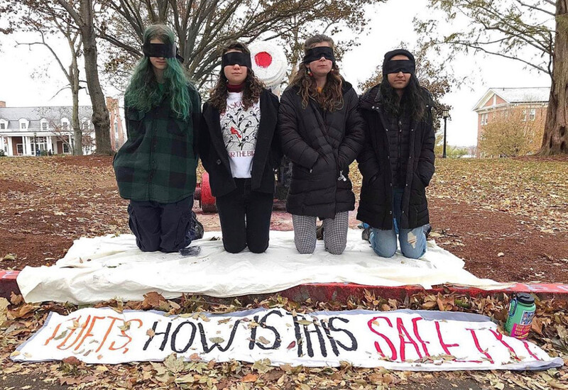 Blindfolded protesters kneel next to a banner.