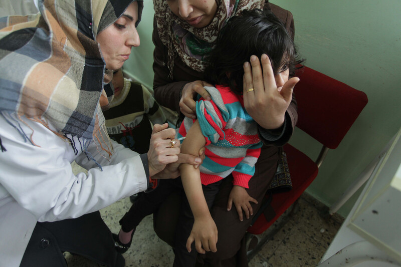 A nurse injects a young child whose face is diverted by her mother