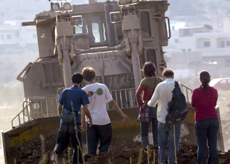 A group of people is dwarfed by a massive armored bulldozer