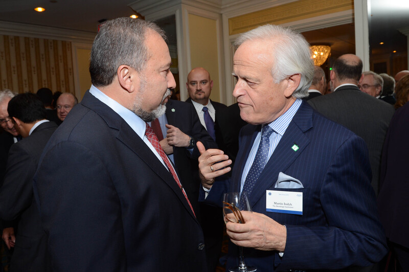 Two men talk together at conference with people in background 