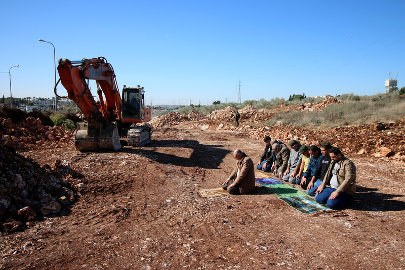 Men pray near construction equipment