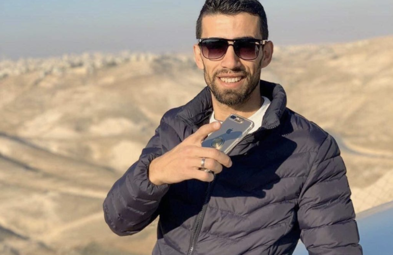 Man smiles and holds phone against backdrop of mountains