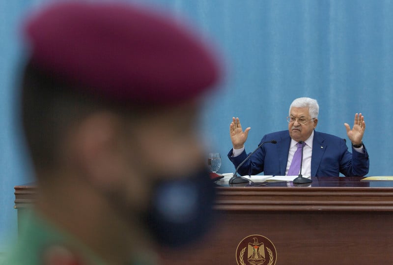 Mahmoud Abbas gestures behind the blurred profile of a Palestinian security officer