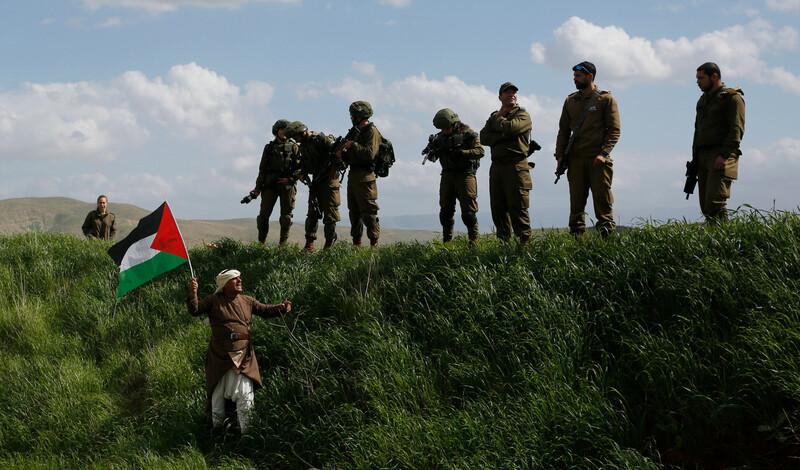 A man waves a Palestinian flag in front of a group of Israeli soldiers