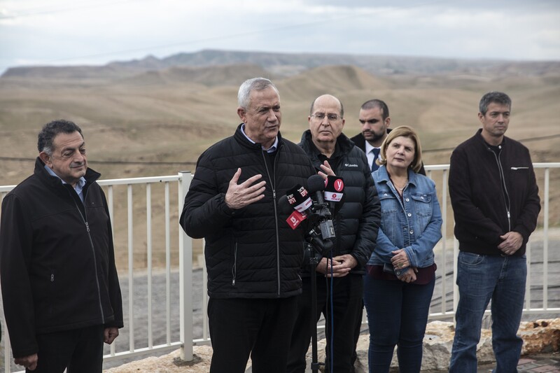 A man talks into several microphones in front of a view of several hills stretching into the distance