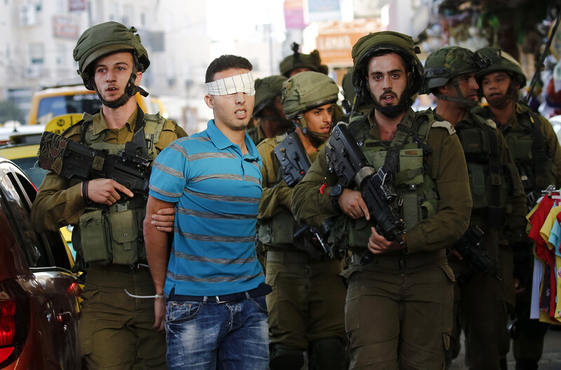 Soldiers restrain a blindfolded youth